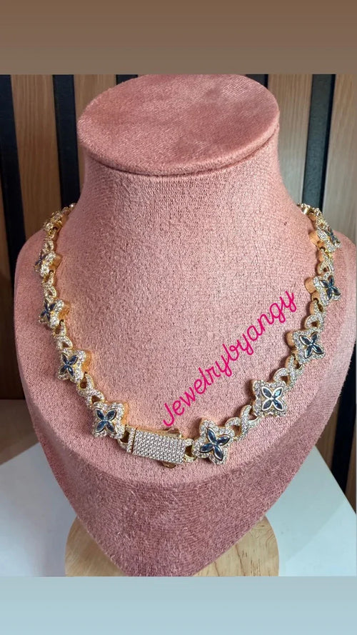 Collar dorado con dijes de flores y circonias, exhibido en busto rosa, joyería elegante.