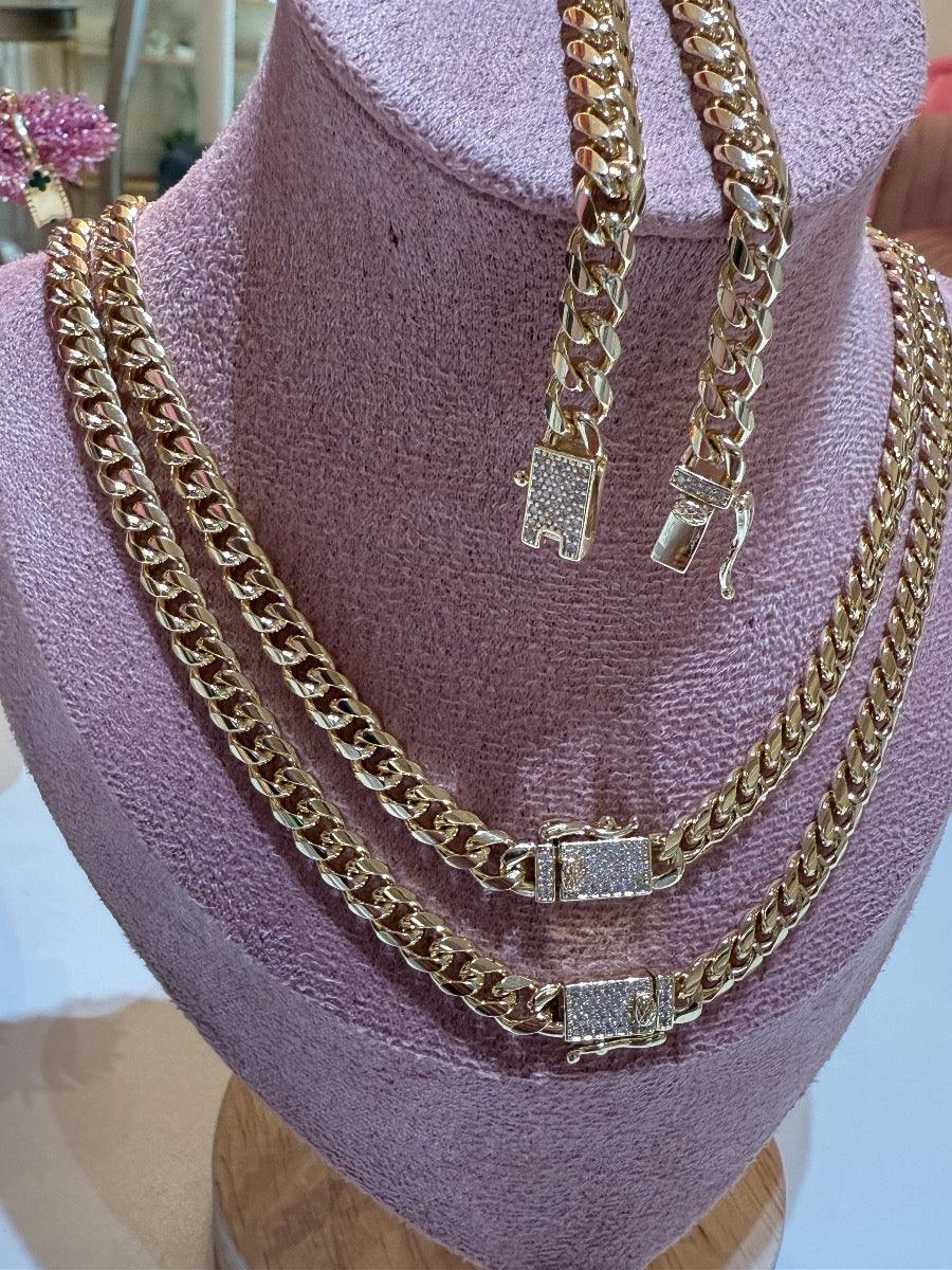 Juego de cadenas y pulsera tipo cubana doradas con broche de brillantes sobre exhibidor