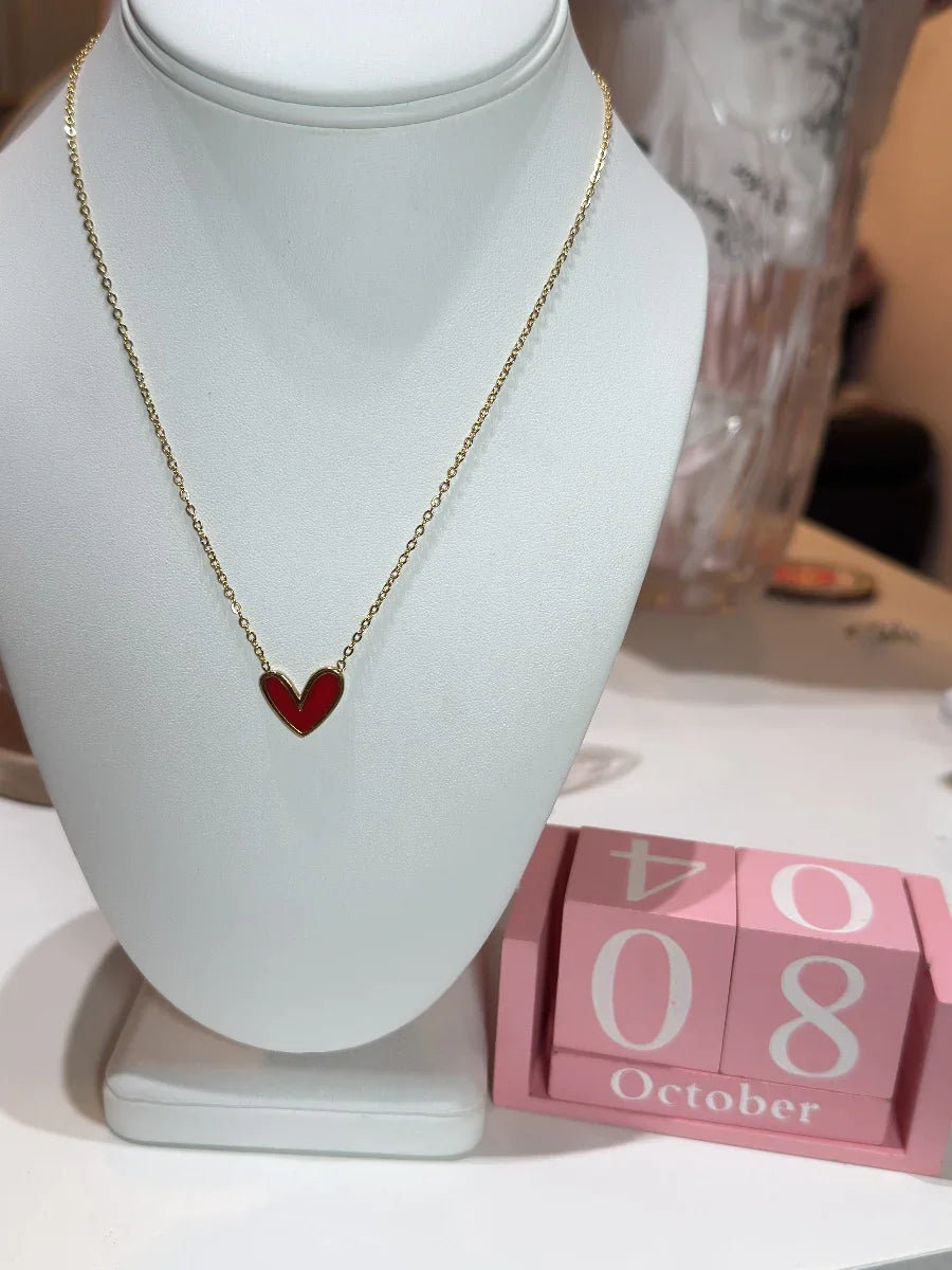 Collar dorado con dije de corazón rojo en exhibidor, ideal para regalo, joyería elegante.