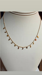 Collar de cadena dorada con dijes de relámpagos, lunas y estrellas, exhibido en busto.