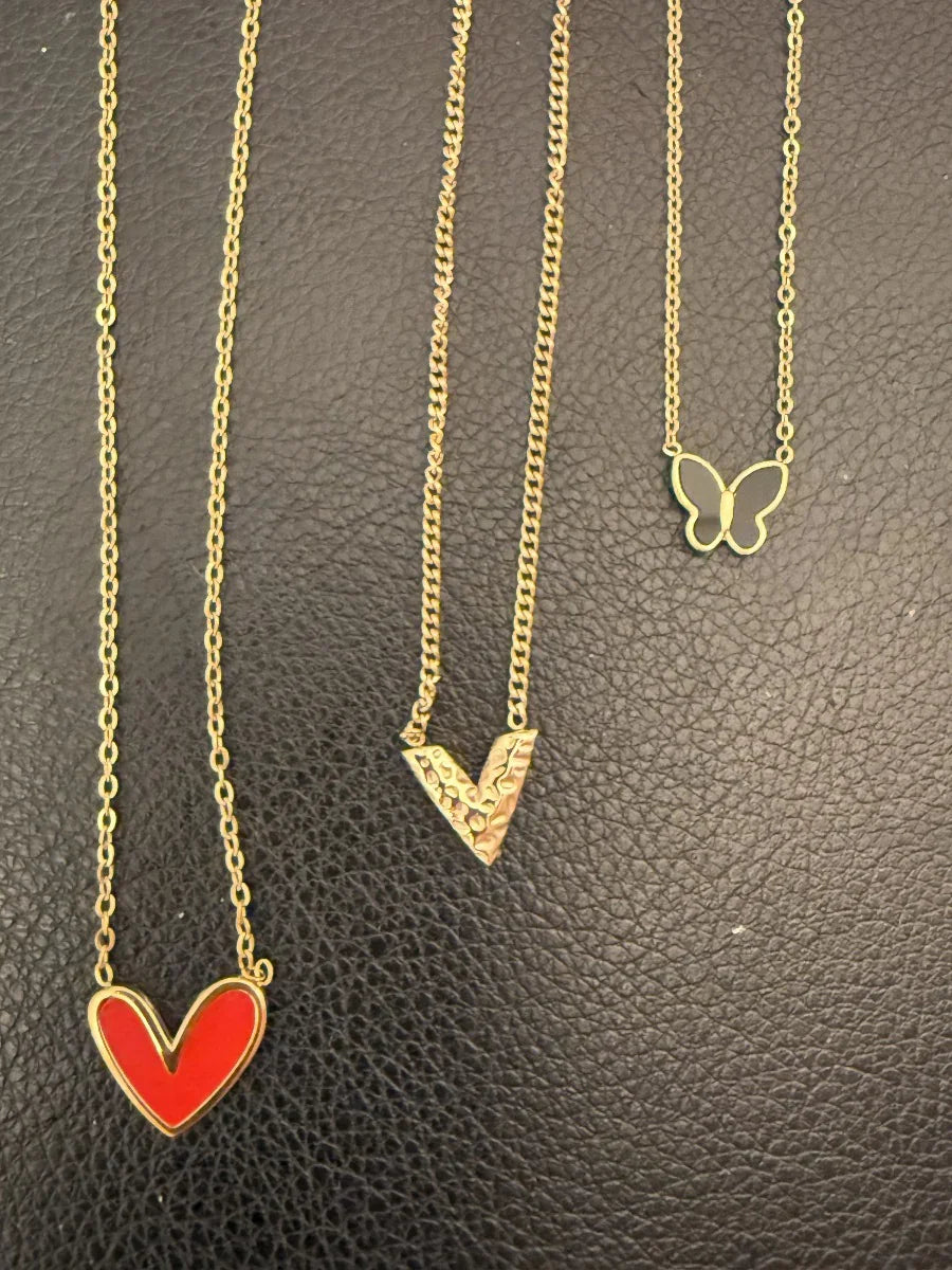 Collares dorados con dijes de corazón rojo, letra V y mariposa sobre fondo negro