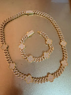 Set de collar y pulsera de cadena dorada con dijes de trébol y circonias sobre fondo dorado