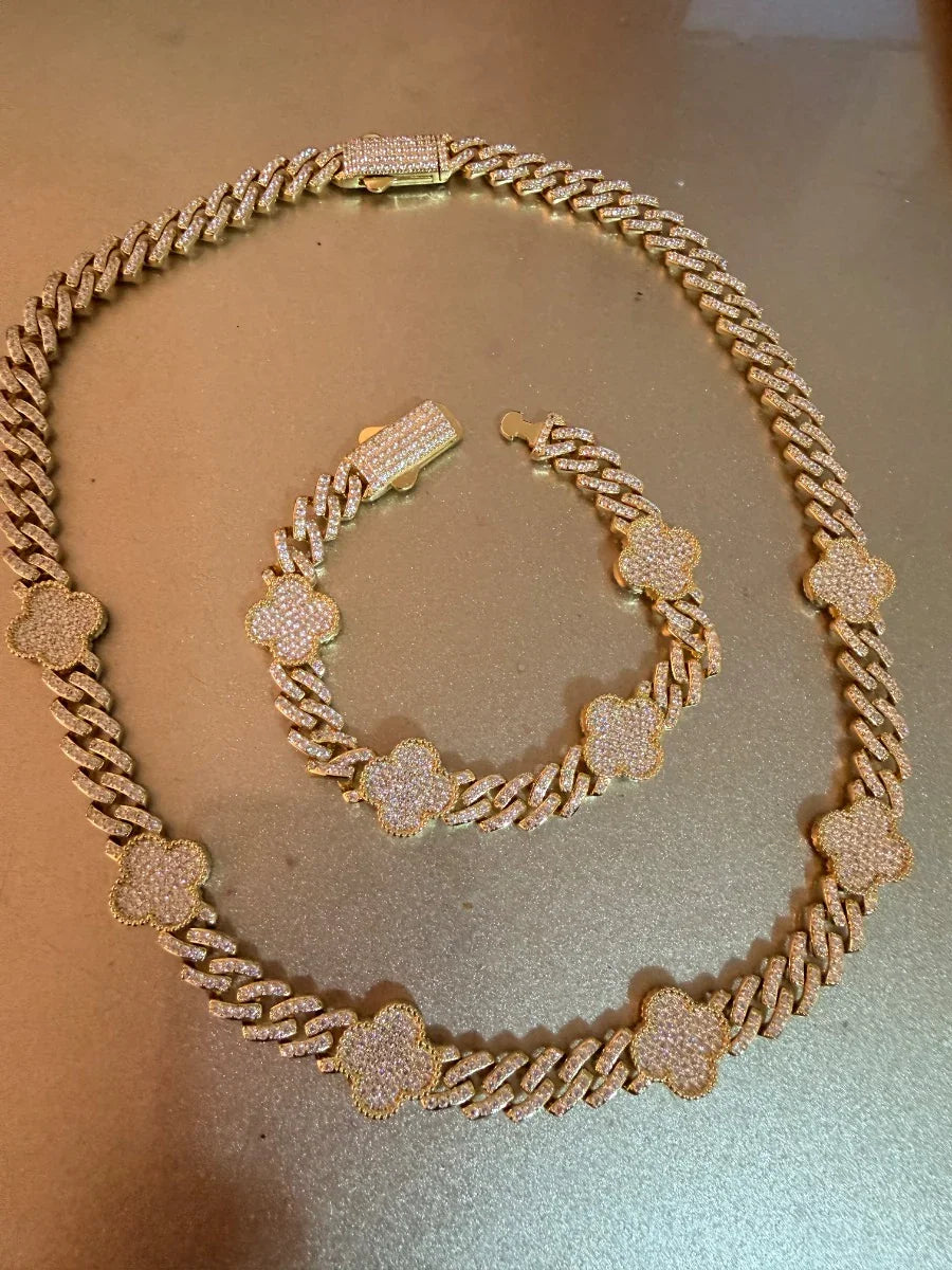 Set de collar y pulsera de cadena dorada con dijes de trébol y circonias sobre fondo dorado