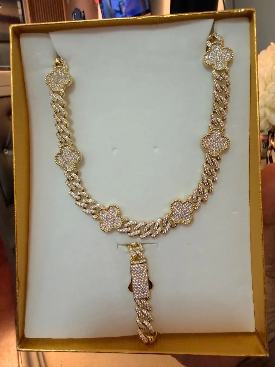 Set de collar y pulsera dorados con tréboles incrustados de circonias, exhibidos en estuche.