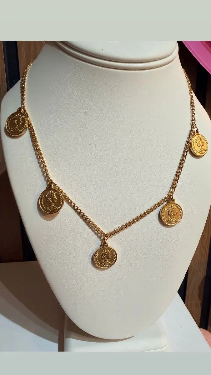 Collar dorado con dijes de monedas, joyería elegante exhibida en busto blanco