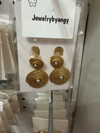 Aretes dorados redondos con textura y perla central, exhibidos en soporte de tienda.