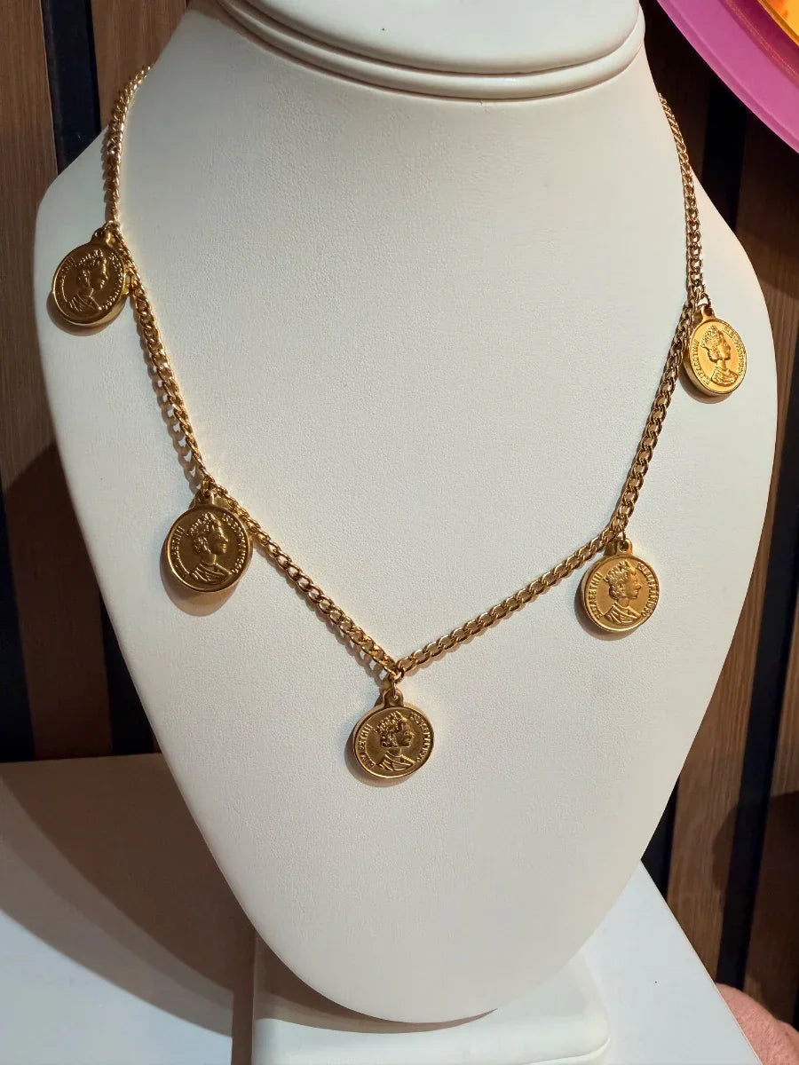 Collar dorado con colgantes de monedas, joyería elegante exhibida en busto blanco.