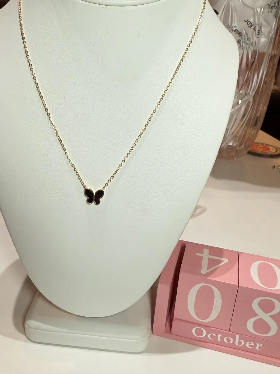 Collar dorado con dije de mariposa negra, exhibido en busto, decoración de calendario rosa.