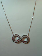 Collar de plata con dije de infinito decorado con piedras brillantes, fondo neutro.