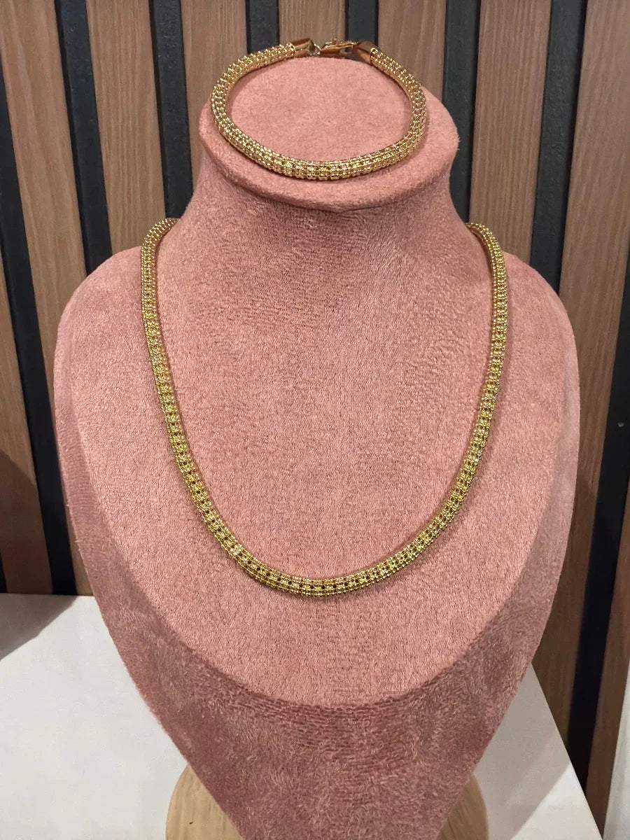 Set de collar y pulsera dorada de malla fina sobre exhibidor rosa, joyería elegante