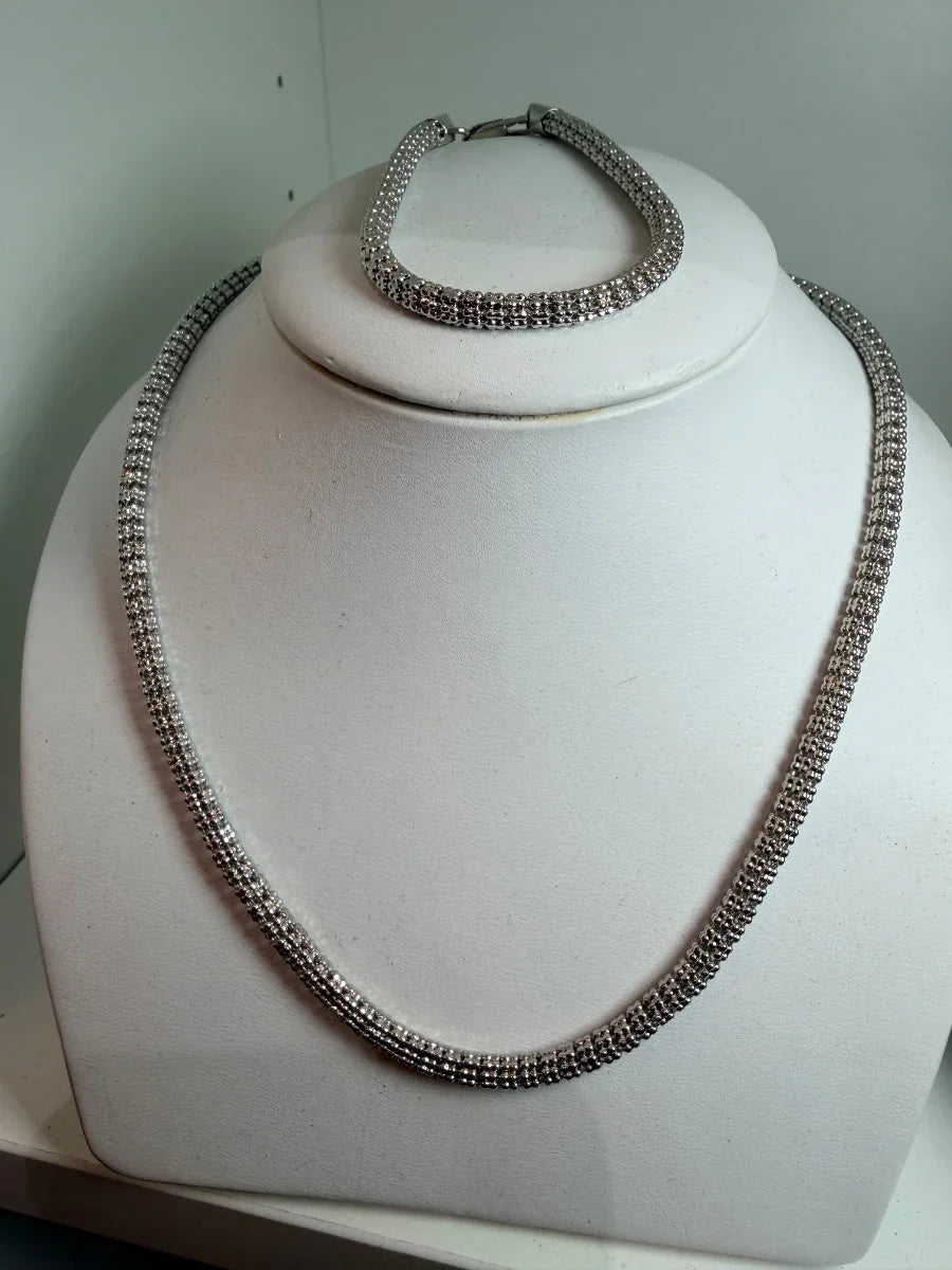 Set de collar y pulsera plateados con brillantes, exhibidos en busto blanco