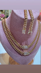 Set de cadenas y pulsera cubanas en oro con broches de circonias, exhibidas en busto rosa.