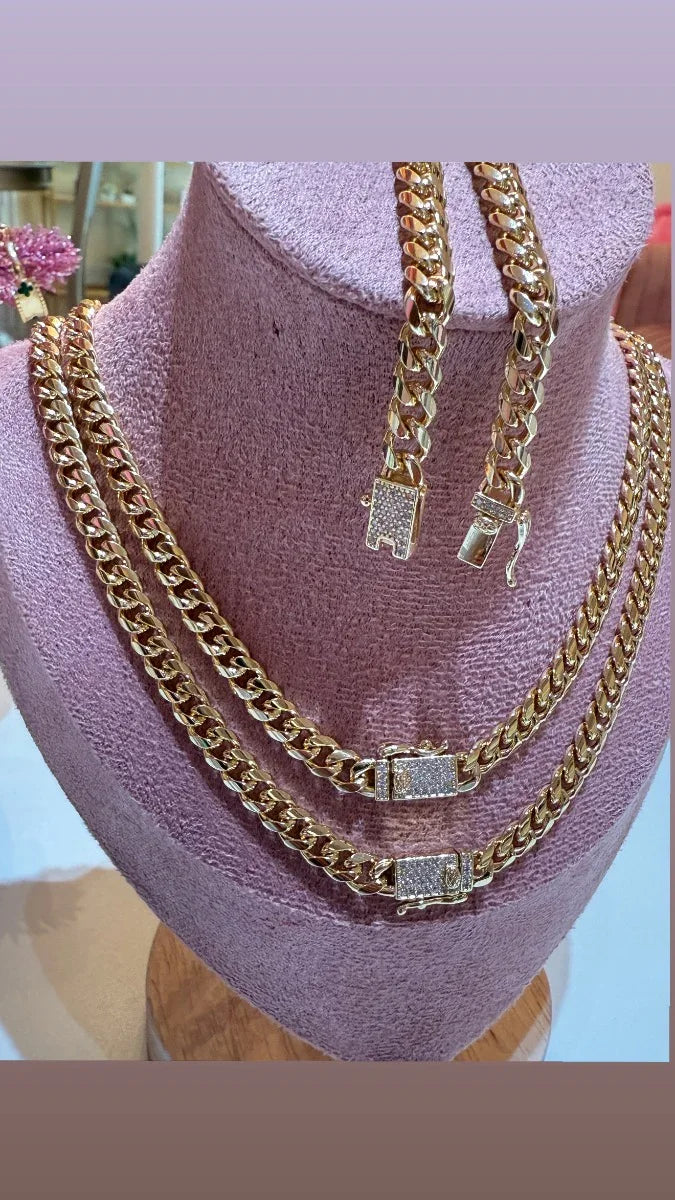 Set de cadenas y pulsera cubanas en oro con broches de circonias, exhibidas en busto rosa.