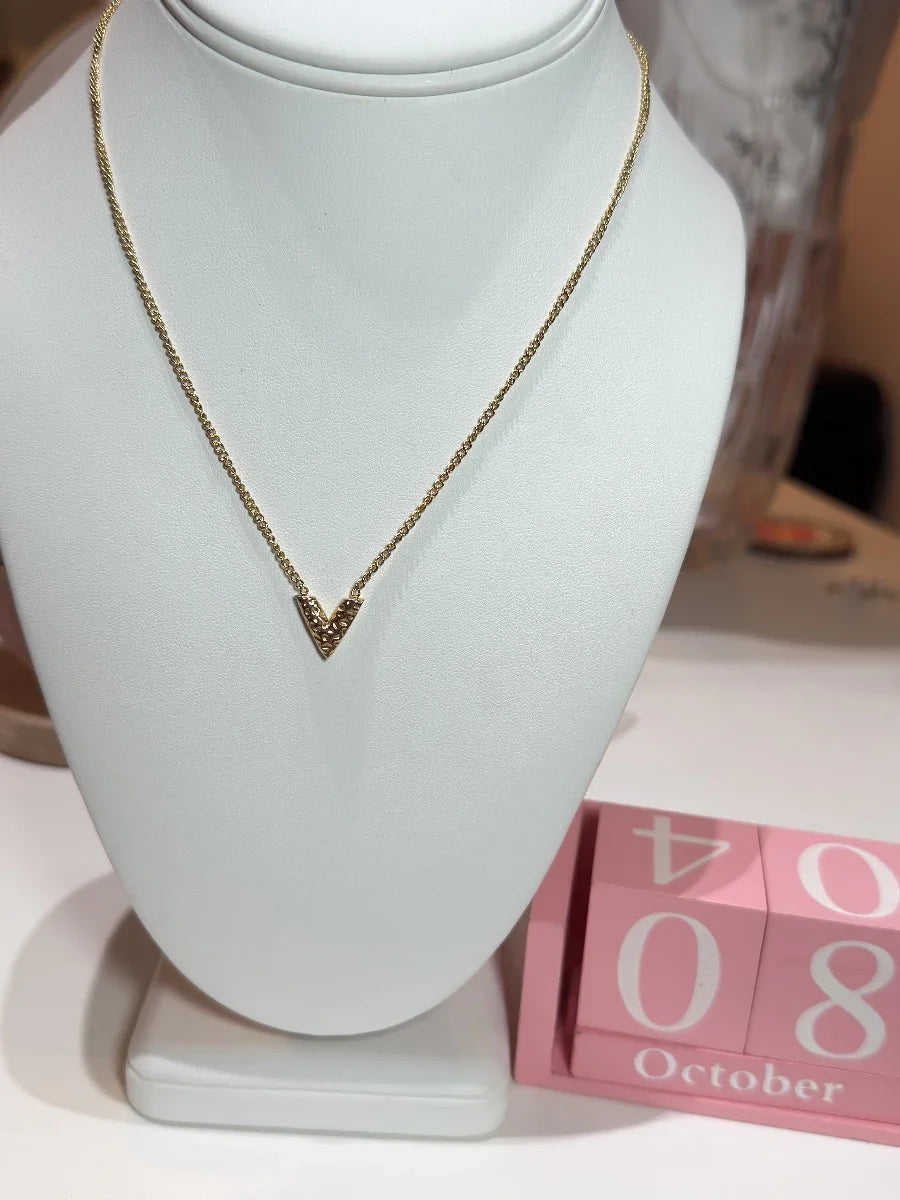 Collar de oro con dije en forma de V sobre exhibidor blanco, fondo con calendario octubre 8