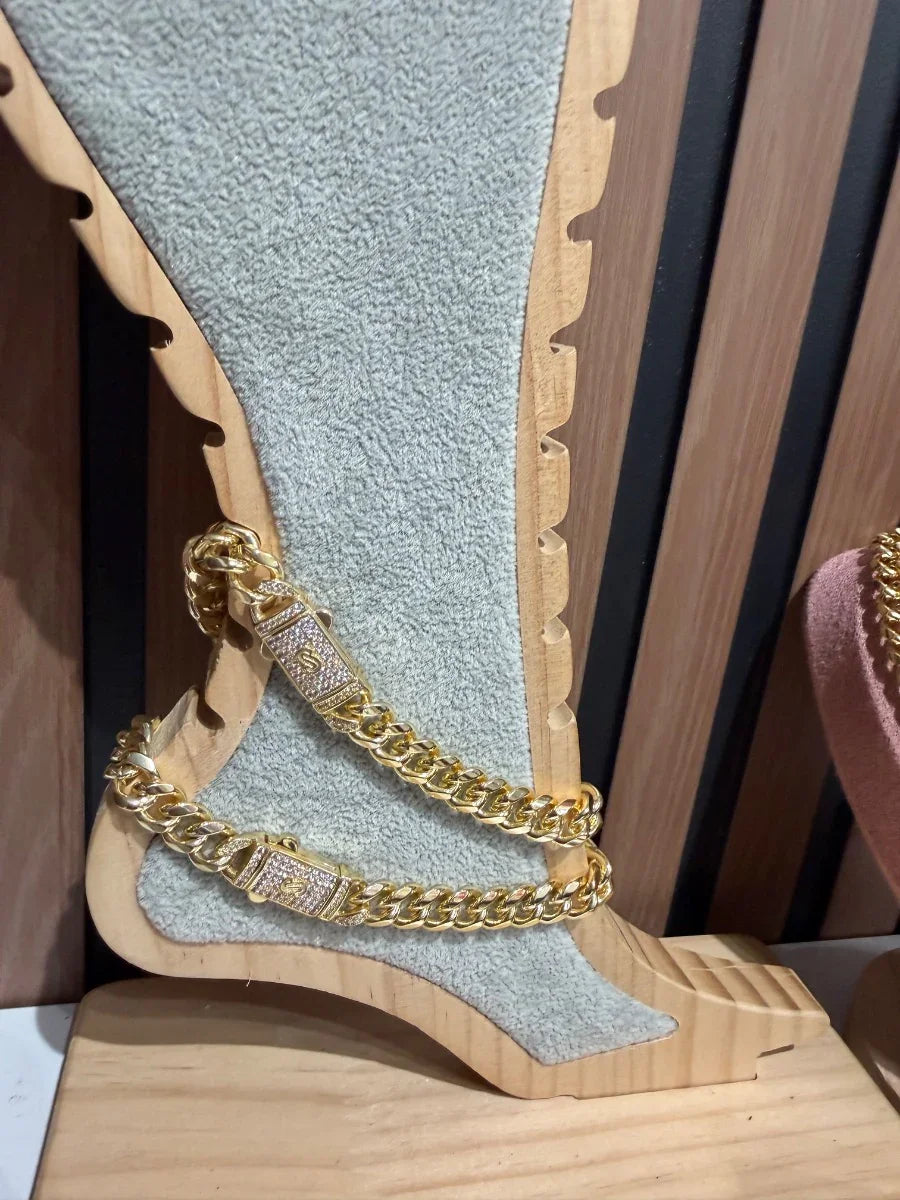 Tobillera de cadena gruesa dorada con broches brillantes sobre exhibidor de madera