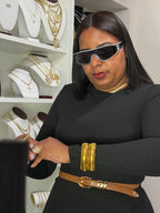 Mujer con gafas de sol, vestido negro y joyería dorada, en tienda de collares y pulseras.