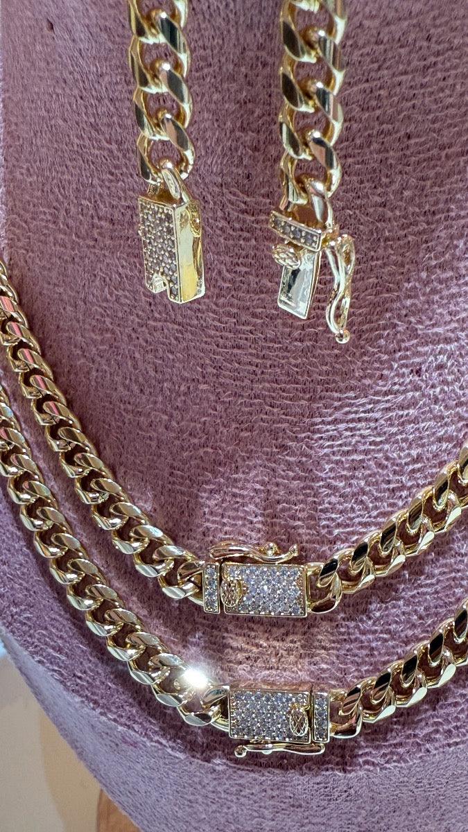 Cadena tipo cubana dorada con cierres de brillantes sobre fondo rosa, joyería elegante