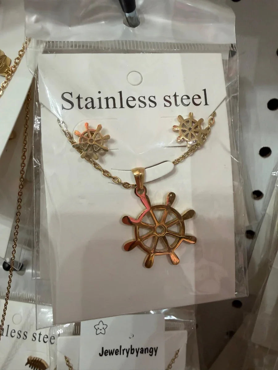 Conjunto de collar y aretes de acero inoxidable dorado con diseño de timón náutico.