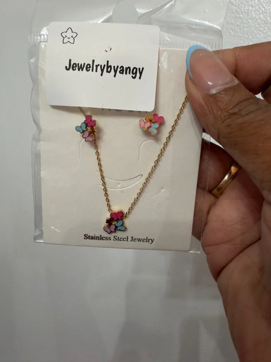 Set de collar y aretes de acero inoxidable con flores coloridas, fondo blanco, mano sosteniendo el empaque.