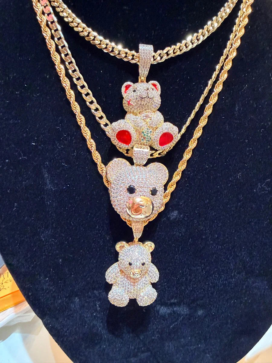 Collares dorados con dijes de osos brillantes y pedrería roja sobre fondo negro.