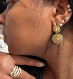 Mujer con aretes dorados texturizados y anillo dorado, joyería elegante.