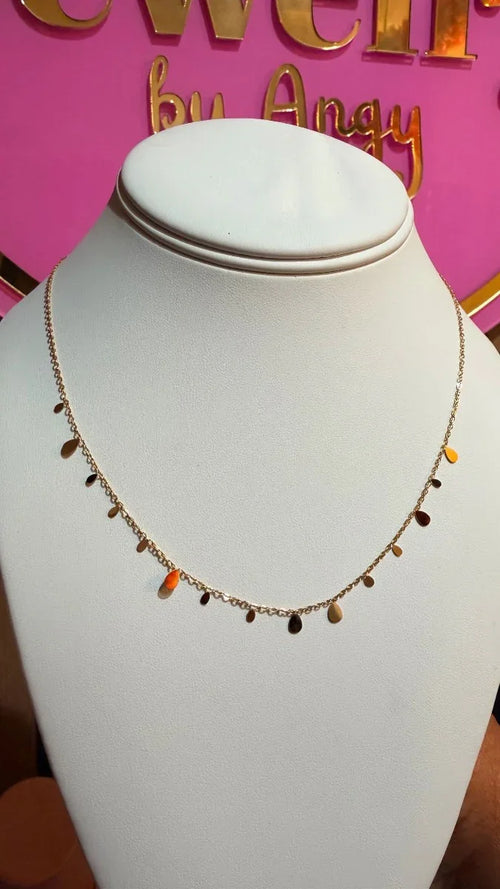 Collar delicado de cadena dorada con dijes colgantes pequeños, exhibido en busto blanco.