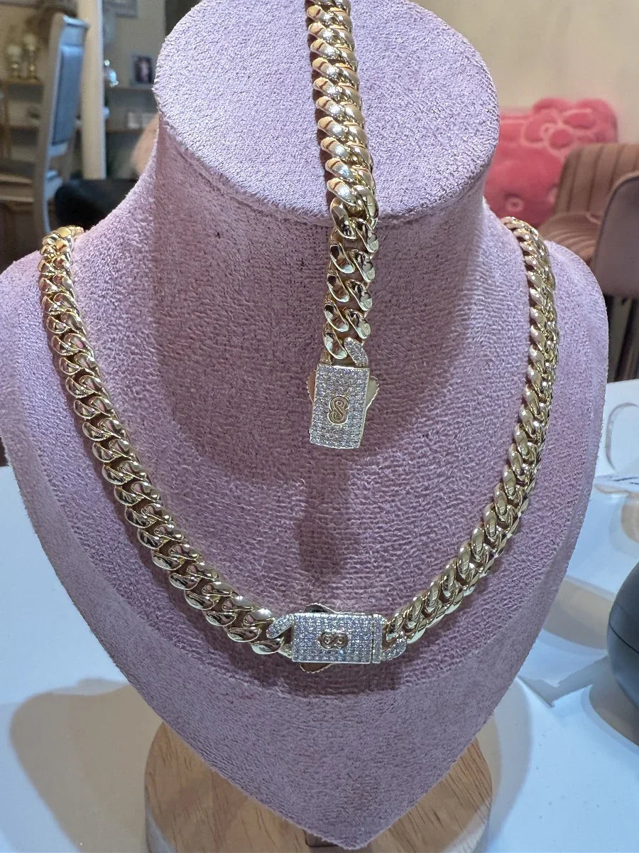 Set de cadena y pulsera tipo cubana doradas con broche brillante, exhibidas en busto lila.