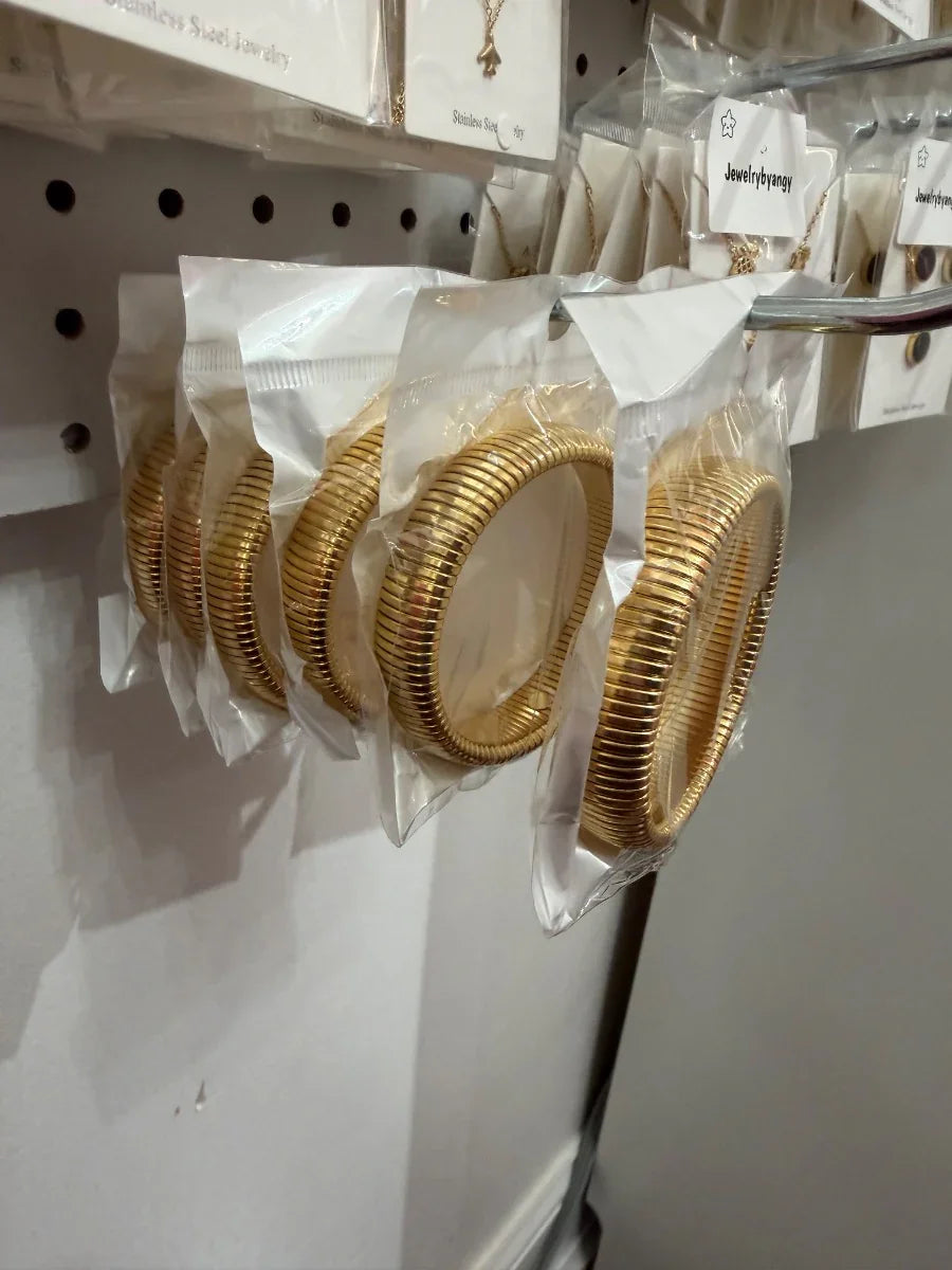 Pulseras doradas de acero inoxidable empaquetadas, exhibidas en pared de tienda de joyería