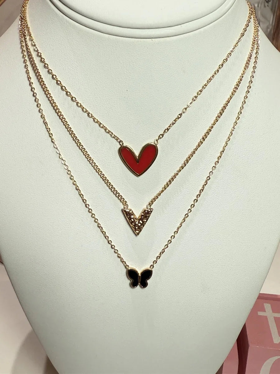 Collar triple de oro con dije de corazón rojo, letra V dorada y mariposa negra.